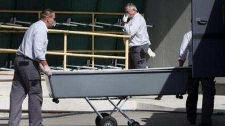 Un ataúd vacío es descargado de un camión fuera del edificio en el que se encuentran los cuerpos de los refugiados fallecidos