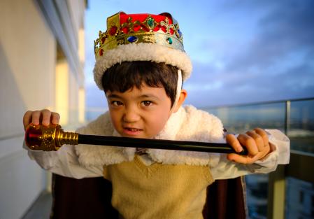 A young boy dressed as a King, wearing a crown, cape and carrying a sceptre.