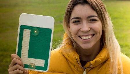 Una joven muestra la placa de conductora novel tras sacarse el carnet de conducir