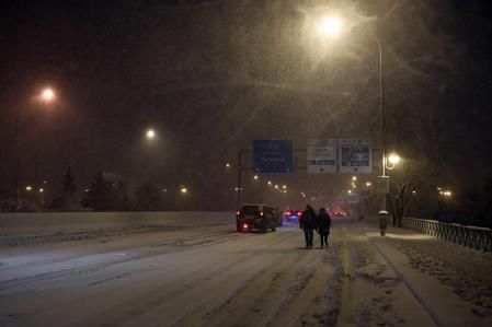 Some people walk as vehicles remain stuck in a road in Madrid due to a heavy snow storm on January 8, 2021. - Heavy snow fell across much of Spain today, leaving huge areas blanketed in white as Storm Filomena brought wintry weather not seen in decades to the Iberian peninsula. The intense snow cut off Madrid's two ringroads, the M30 and the M40, and a red alert was declared in the city centre where police were struggling to help people stranded in vehicles. (Photo by OSCAR DEL POZO / AFP)