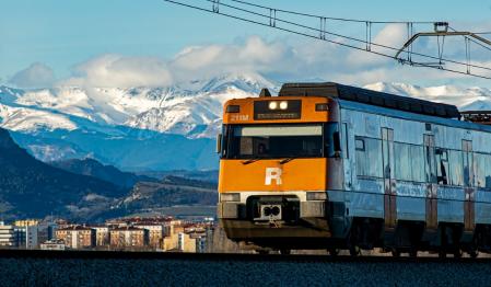 El tren de Vic avanza con los Pirineos nevados de telón de fondo.