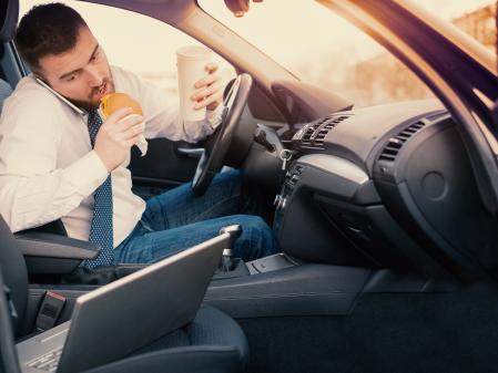 Man eating an hamburger and working seated in his car