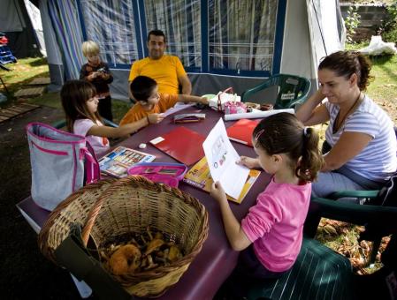Niños hacen deberes junto a sus padres en el exterior de su tienda de campaña en un cámping en Berga. Ayudar está bien, pero no hacer los deberes por ellos