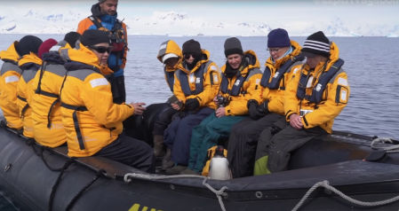 Imagen del pingüino encima del bote con todos los turistas sorprendidos con su presencia.