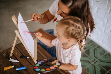 Mother reaching her daughter how to paint on canvas