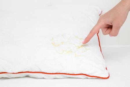 Woman's hand finger pointing to saliva stain on white pillow. Cleaning problem and solution concept. Closeup.