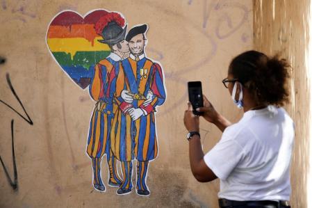 Una mujer fotografía un mural de la artista Laika en Roma donde aparecen dos guardias suizos del Vaticano dándose un beso.