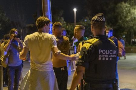 Un agente de la Guardia Urbana y jóvenes abandonando la playa de la Barceloneta la noche en la que entraba en vigor el toque de queda en Catalunya