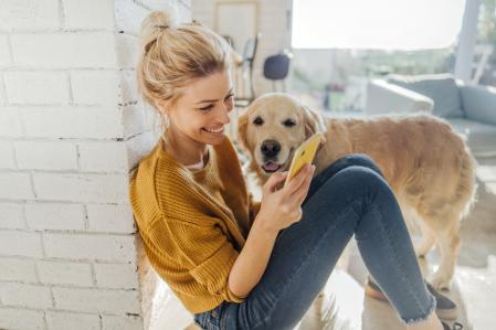 Photo of a young woman reading morning news online while her dog standing next to her