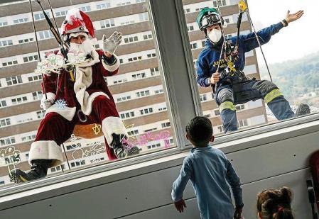 GRAFCAT1028. BARCELONA, 21/12/2021.- El colectivo Bombers Solidaris, con la colaboración de la Fundación Enriqueta Villavecchia, se han deslizado hoy desde la azotea hasta el séptimo piso del Hospital Trias i Pujol de Badalona para que Papa Noel y dos elfos visitasen a los niños ingresados y a los sanitarios. EFE/Enric Fontcuberta