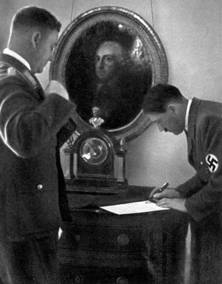 Adolf Hitler, a la derecha, firmando unos documentos. Tras él puede verse un retrato de Federico de Prusia.