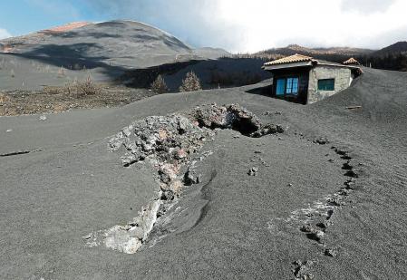 GRAFCAN677. LAS MANCHAS (LA PALMA) (ESPAÑA), 25/02/2022.- Más de dos meses después de que terminara la erupción en Cumbre Vieja, el 13 de diciembre, el color negro lo cubre casi todo en las cotas altas de la localidad de Las Manchas, al sur del cono principal, donde la caída de cenizas fue constante durante los 85 días que se mantuvo activo el volcán. En la imagen, Julio Rodríguez, vecino de Las Manchas, posa junto a su vivienda, donde continúa trabajando en la retirada de cenizas. En la imagen, vivienda en Las Manchas completamente cubierta por la ceniza, con una colada de lava que brotó bajo sus cimientos. EFE/Elvira Urquijo Á.