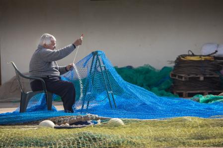 Un hombre remienda una red de pesca en el muelle de pescadores de Barcelona