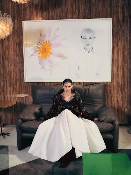 chaqueta biker con peplun de piel negra, falda larga fruncida blanca y botines de tacón negros. Todo de Alexander McQueen . Se sienta en el sofá Maralunga, diseñado por Vico Magistretti. El cuadro se titula Andy dandy (Four) , obra de The Hilton Brohters(2007)