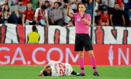 The referee gestures as Sevilla's French forward Anthony Martial (L) lies on the ground during the Spanish League football match between Sevilla FC and Real Madrid CF at the Ramon Sanchez Pizjuan stadium in Seville on April 17, 2022. (Photo by CRISTINA QUICLER / AFP)