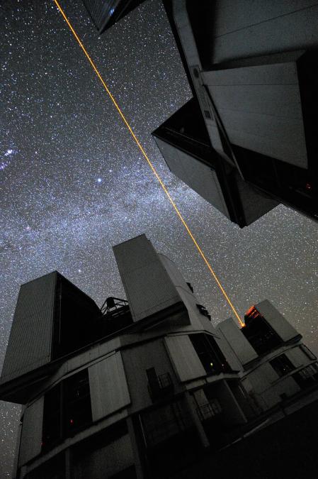 Esto es más o menos lo que podríamos ver si nos tumbásemos sobre la plataforma del VLT de noche, cuando se utiliza la estrella láser guía (LSG). El rayo láser, lanzado desde el telescopio Yepun de 8,2 metros del VLT, cruza el cielo y crea una estrella artificial a 90 km de altitud, en la mesosfera alta de la Tierra. El LGS es parte del sistema de óptica adaptativa del VLT y se utiliza como referencia para corregir las aberraciones que causa la atmósfera en las imágenes. En esta impactante fotografía, pueden verse tres de los cuatro telescopios de 8,2 metros del VLT. La Vía Láctea, con la brillante estrella Sirio en el centro, aparece casi perpendicular a la dirección del láser. En el borde izquierdo podemos ver la espada de la constelación de Orión; el brillante punto difuso es la región de formación estelar M 42, más conocida como la nebulosa de Orión.