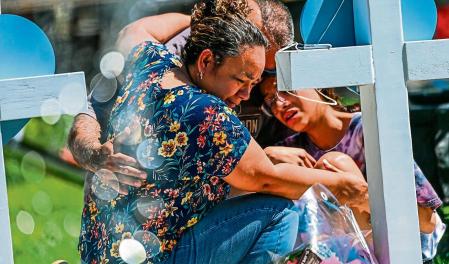 TOPSHOT - People mourn at a makeshift memorial outside Uvalde County Courthouse in Uvalde, Texas, on May 26, 2022. - Texas police faced angry questions May 26, 2022 over why it took an hour to neutralize the gunman who murdered 19 small children and two teachers in Uvalde, as video emerged of desperate parents begging officers to storm the school. (Photo by CHANDAN KHANNA / AFP)