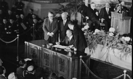 Dean Acheson, secretario de Estado de Estados Unidos, firma el acuerdo de constitución de la Organización del Tratado del Atlántico Norte en presencia del presidente Harry Truman, de pie en el centro