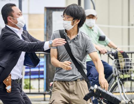 Tetsuya Yamagami, left, holding a weapon, is detained near the site of gunshots in Nara, western Japan Friday, July 8, 2022. Former Prime Minister Shinzo Abe was assassinated Friday on a street in western Japan by Yamagami, a gunman who opened fire on him from behind as he delivered a campaign speech — an attack that stunned the nation that has some of the strictest gun control laws anywhere.(Nara Shimbun/Kyodo News via AP)