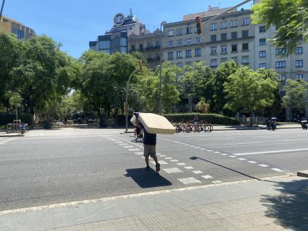 Un hombre sin hogar en la calle Aragó trasladando el colchón que usa para dormir