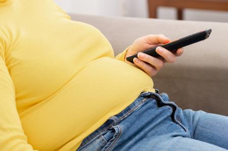 Side view of young obese woman relaxing on sofa and watching tv