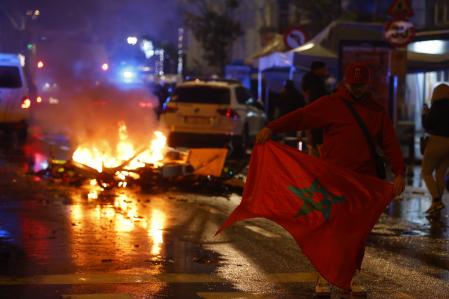 Un hombre con la bandera de Marruecos pasa por delante de un vehículo incendiado