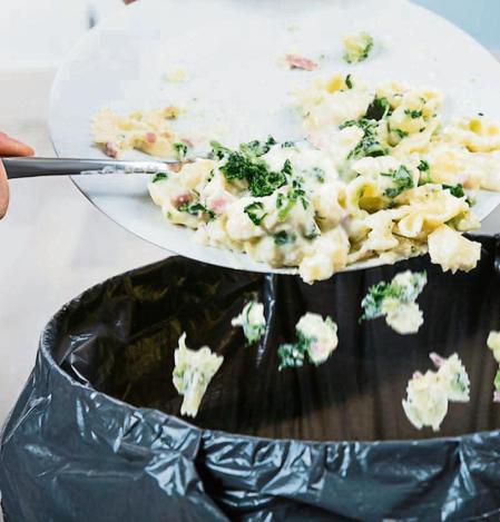 Close-up Of A Person Throwing The Leftover Pasta Into The Trash Bin