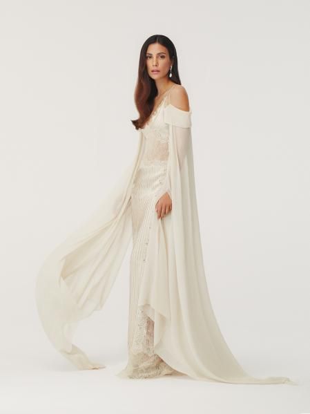 Impactante vestido columna de estilo lencero, realizado con nervios de raso de seda con manipulaciones de encaje e8, unidas con microajours. El encaje en el busto y en los costados dibuja un delicado motivo floral cosido en nervaduras, elevando la silueta y jugando con las transparencias. Tirantes finos 100% de seda. Mangas extralargas desmontables de georgette de seda que evocan una sensación flotante cuando están en movimiento. Pendientes de plata con perlas y zapatos con pedrería de Fendi Haute Couture