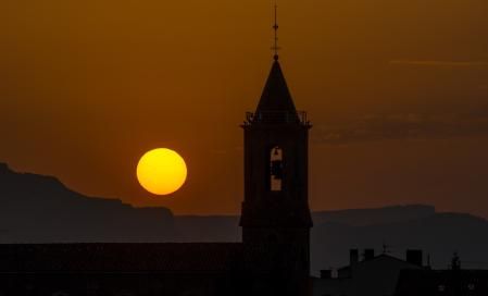 El sol entre el horizonte y el campanario de la iglesia de Sentfores.