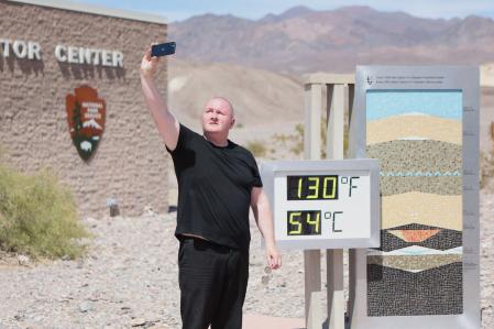 Scott Hughes, of Swansea, Wales, UK, takes a selfie next to a digital display of an unofficial heat reading at Furnace Creek Visitor Center during a heat wave in Death Valley National Park in Death Valley, California, on July 16, 2023. Tens of millions of Americans braced for more sweltering temperatures Sunday as brutal conditions threatened to break records due to a relentless heat dome that has baked parts of the country all week. By the afternoon of July 15, 2023, California's famous Death Valley, one of the hottest places on Earth, had reached a sizzling 124F (51C), with Sunday's peak predicted to soar as high as 129F (54C). Even overnight lows there could exceed 100F (38C). (Photo by Ronda Churchill / AFP)
