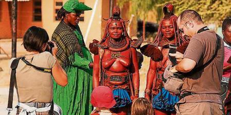 Un grupo de turistas fotografiando a tres mujeres himbas, en Opuwo, Namibia