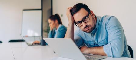 Exhausted young businessman using laptop at work and sitting by the desk while