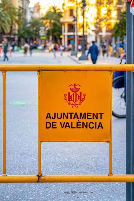 Valencia, Spain - April 15, 2022: A metallic barrier with the coat of arms of the city is seen in the old town. Incidental people walk in the background.