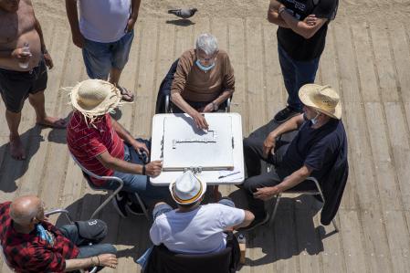 Un grupo de hombres se distrae jugando al domino protegidos con sombrero junto al mar en el barrio de la Barceloneta