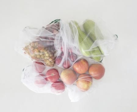 Top view of fruits and vegetables in reusable net bags. Eco friendly and zero waste organic cotton mesh for food storage and shopping
