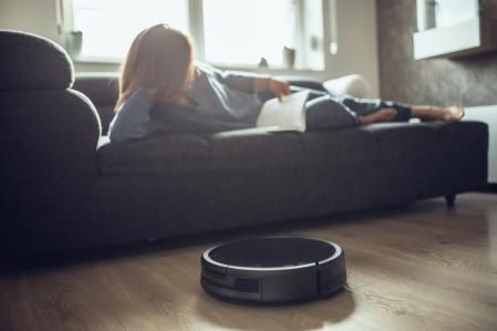 Robotic Vacuum Cleaner Cleaning Floor While Woman reading book
