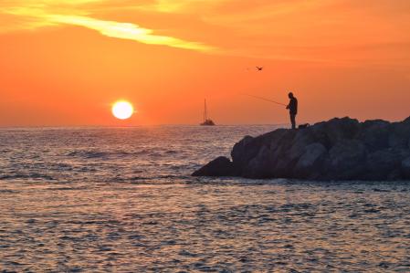 Pescando al amanecer en el espigón de Fuengirola con el cielo arrebolado.