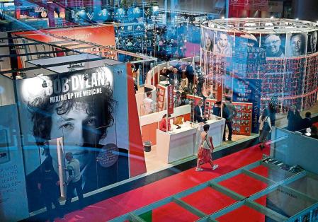 A general view taken through a window screen on October 19, 2023 shows visitors walking past a booth promoting the book by Mark Davidson and Parker Fishel 'Bob Dylan: Mixing Up the Medicine' at The Frankfurt Book Fair in Frankfurt am Main, western Germany. The 75th edition of The Frankfurt Book Fair takes place until October 22, 2023. (Photo by Kirill KUDRYAVTSEV / AFP)