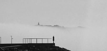 El espigón del puerto de L'Estartit, pero la niebla únicamente deja ver la cima de la Meda Gran.