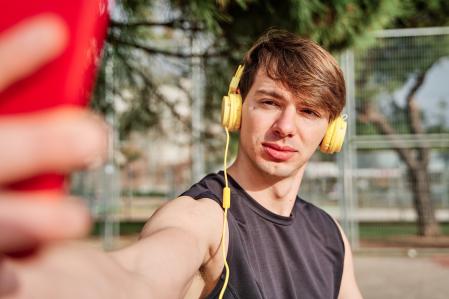Cheerful young sportsman making video call on his smartphone with earphone - young fit male taking a selfie after exercising