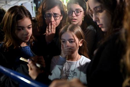 Una madre y sus hijos reaccionan ante la noticia de que Hanna Katzir, quien según la Jihad Islámica murió en cautiverio, se encuentra entre los 13 israelíes liberados mientras ven en su teléfono cómo los rehenes son liberados en Egipto antes de ser llevados a Israel por el CICR, fuera del Museo de Tel Aviv