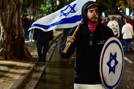 A protester carries a national flag during a rally for supporters and relatives of Israeli hostages held in Gaza since the October 7 attack, in Tel Aviv on December 23, 2023, amid ongoing battles between Israel and the Palestinian group Hamas. (Photo by Alberto PIZZOLI / AFP)