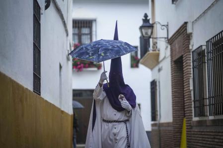 Un nazareno de la Hermandad de La Pasión se cubría en 2024 con un paraguas el Miércoles Santo a la espera de la suspensión por lluvia de su estación de penitencia&nbsp;