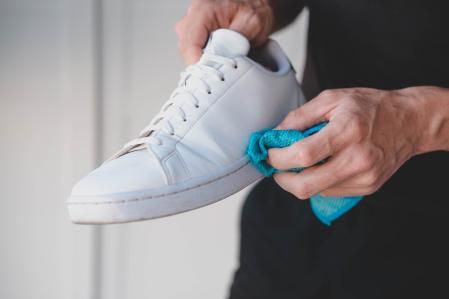 A man cleans white sneakers from dirt