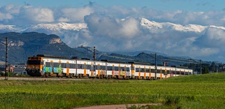 El tren de Rodalies en la Plana de Vic con las montañas nevadas al fondo.