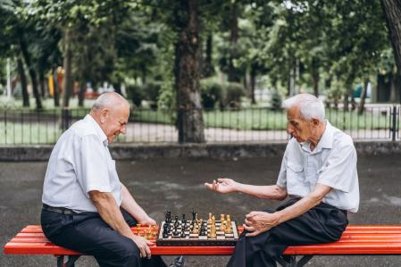 Two senior adult men playing chess on the bench outdoors in the park