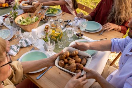 Hands of people passing tray of baked potatoes over dinner table with tasty food, view from above