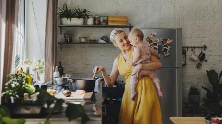 Una madre sonriente sosteniendo a su bebé mientras preparaba el almuerzo en casa