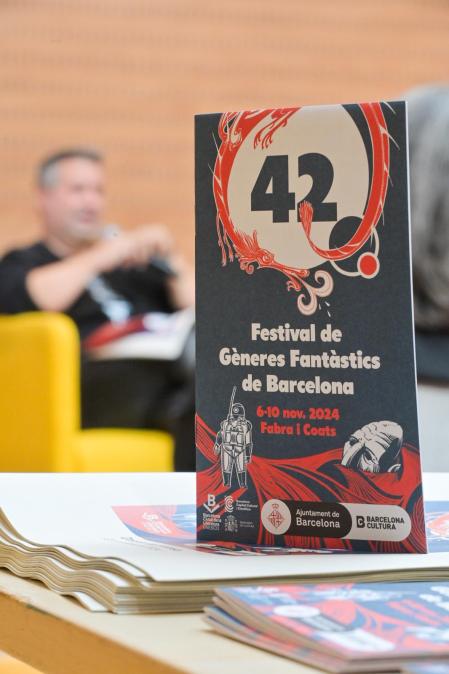 El programa del festival 42, amb il·lustració de Agustín Comotto. De fons, Ricard Ruiz Garzón, comissari del festival, durant la presentació