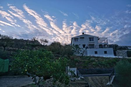 Cielo de borreguitos sobre una casa de Mijas rodeada de huerto y montaña.